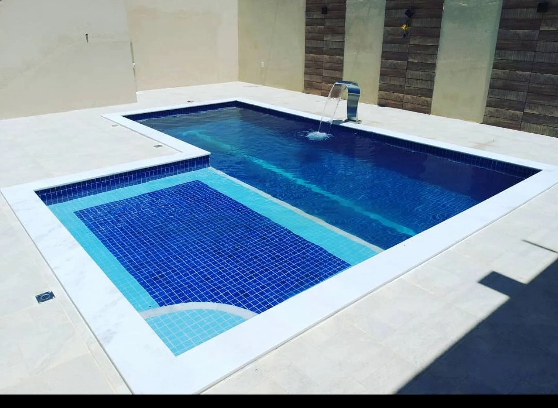 Piscina com pastilhas azuis, degraus submersos, bordas claras e cascata